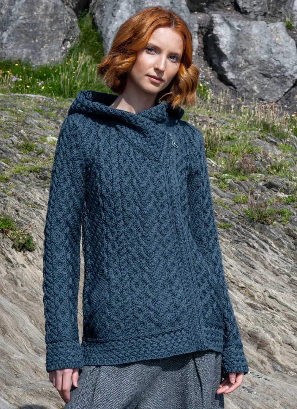 Red headed model standing in rocky area wearing a blue Aran biker hoodie